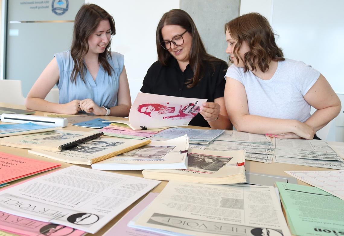 VIU Research Assistant Elise Cullon, Dr. Whitney Wood and Katie Carroll look at historical documents laid out on a desk.