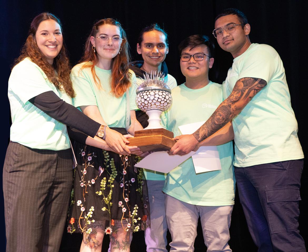 A group of students holds a trophy, all are wearing green shirts