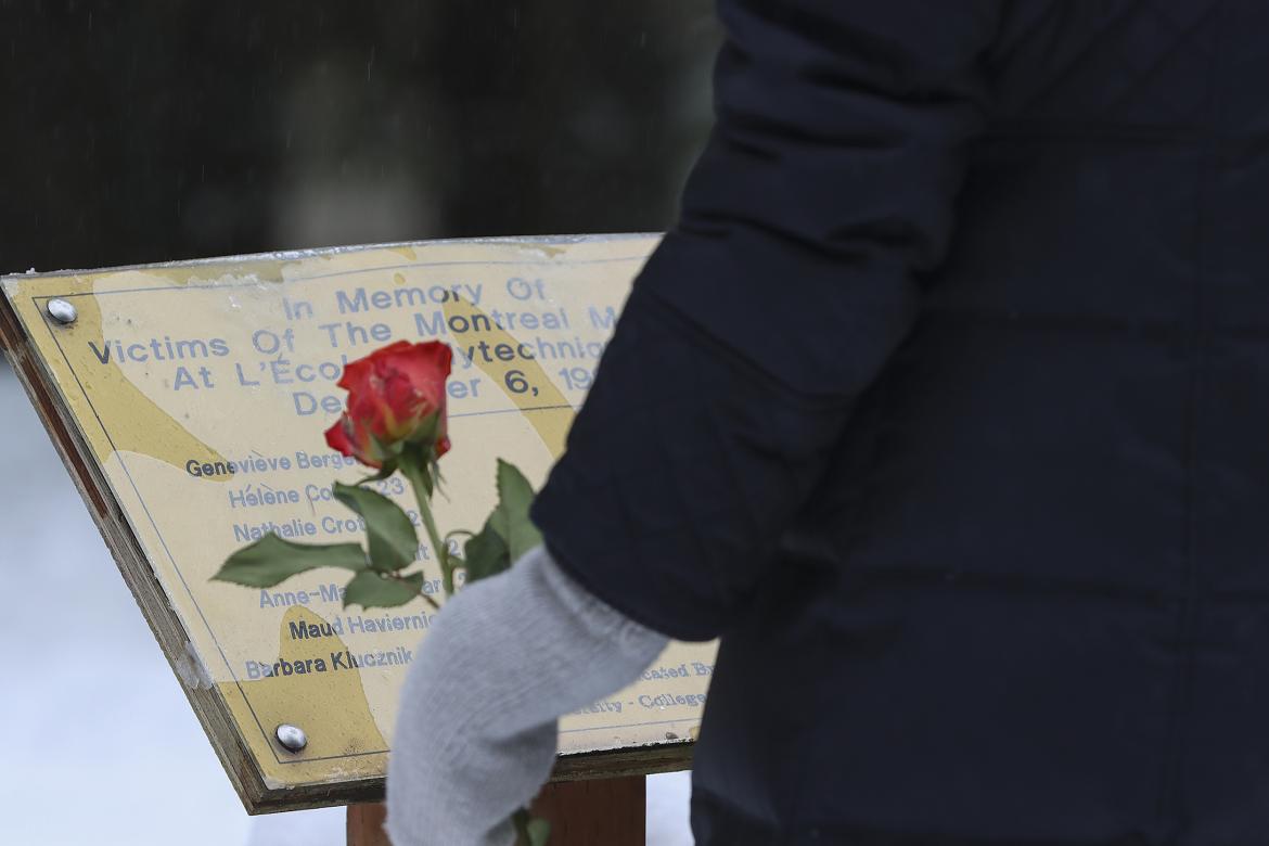 A person holding an orange rose stands in front of the plaque dedicated to the 14 young women who were murdered in the 1989 massacre at École Polytechnique.
