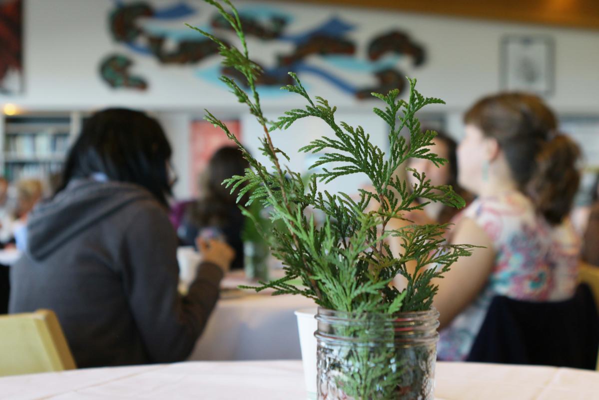 Cedar branch in a jar in foreground, people in VIU's Gathering Place in background
