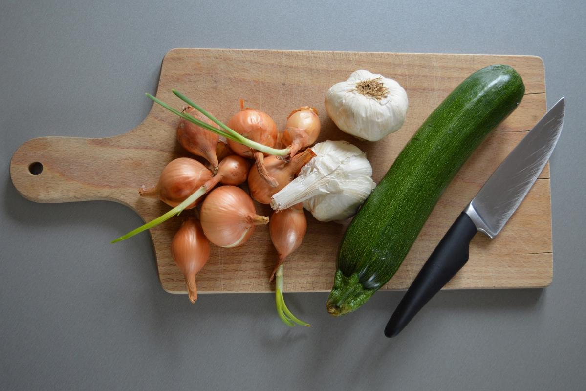 A cutting board with onions, garlic and zucchini