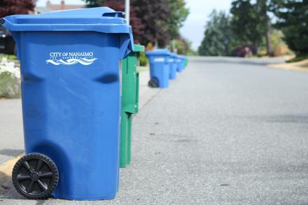 Blue garbage bins and green recycling bins line the left side of a Nanaimo street.