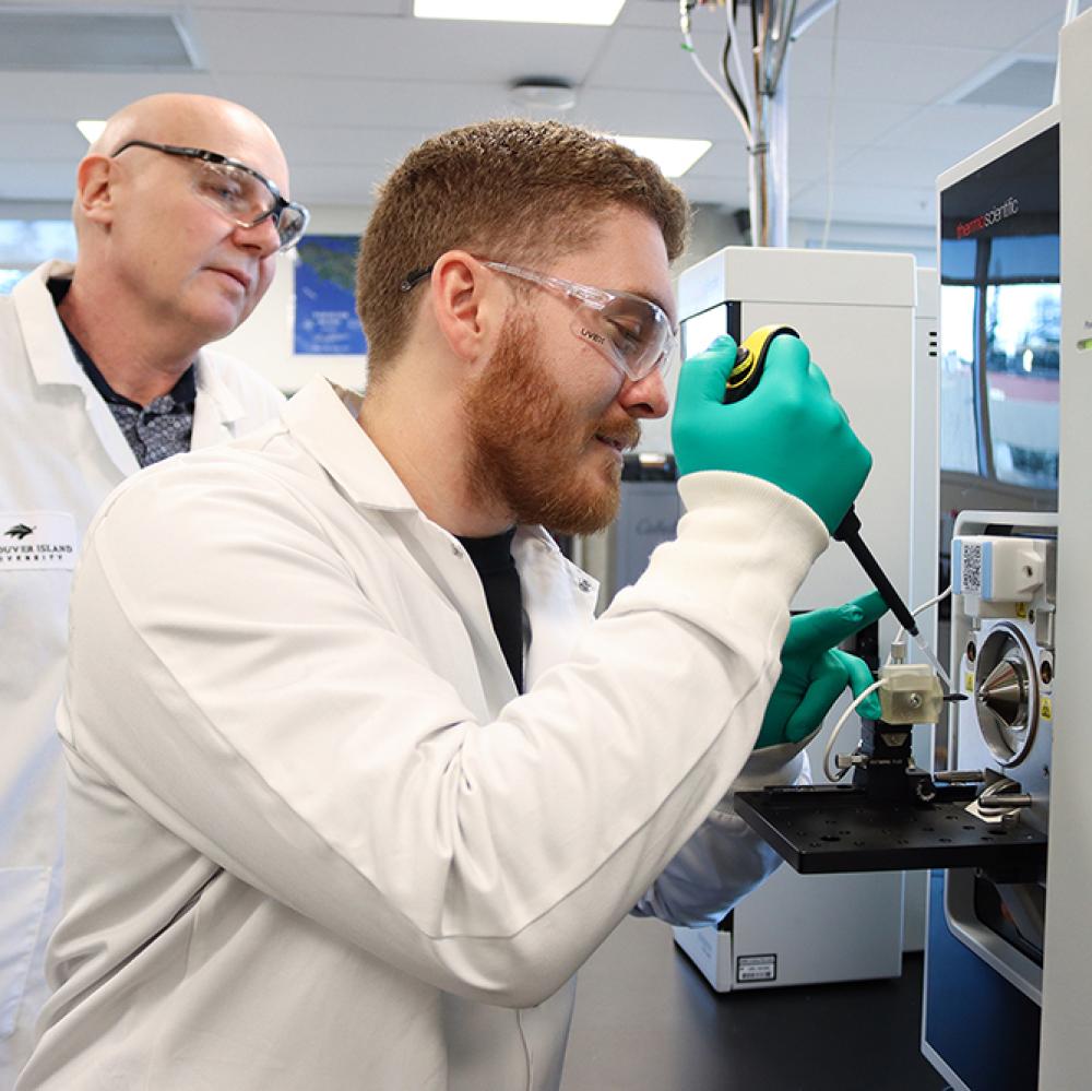 Dr. Chris Gill observes as Lucas Abruzzi puts a sample in the mass spectrometer.